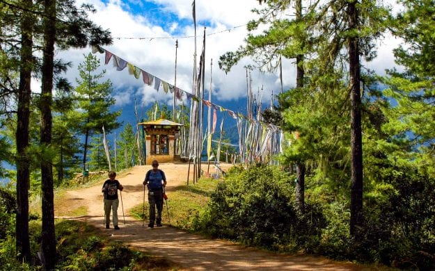 Hikers in Bhutan forest walk beneath colorful flags