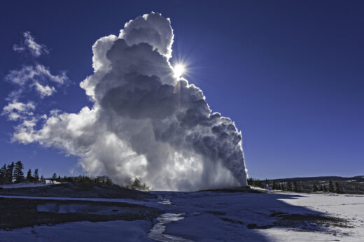 Old Faithful Geyser in the Upper Geyser Basin of Yellowstone National Park in the winter with steam. Sun.