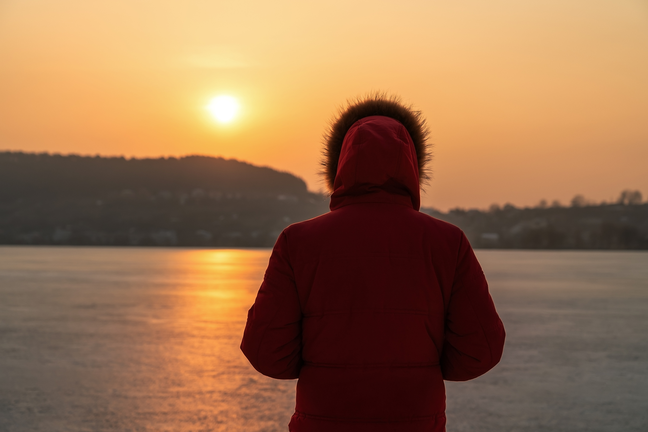 A young man in a red jacket, in the winter on the frozen sea, stands with his back in thought. Against the background of a sunset.