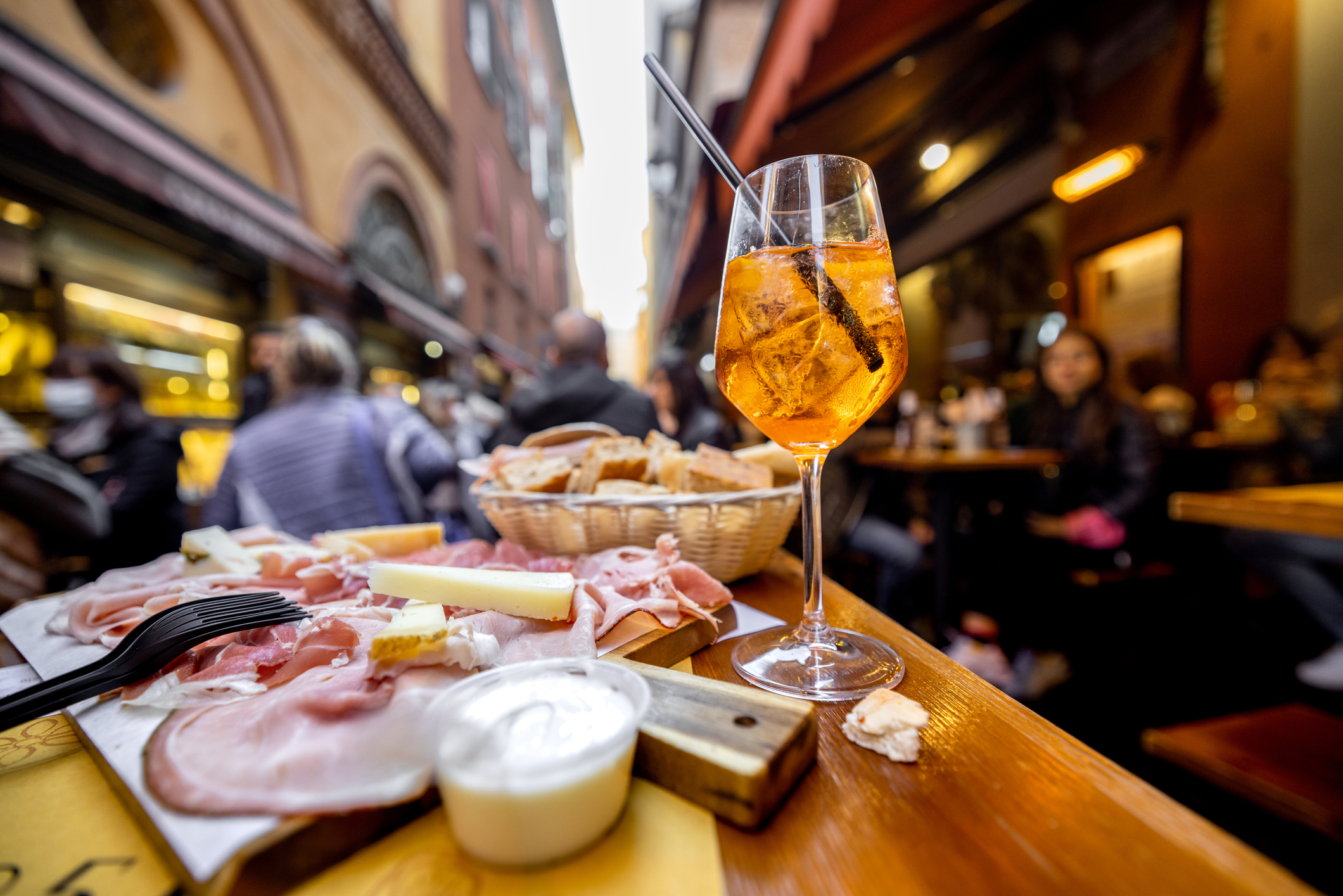 Meat plate with sliced italian sausages, proscutto, cheese, bread and Spritz Aperol drink on a table at outdoor bar on crowded street background